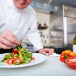 Hands of male chef serving vegetable salad on plate